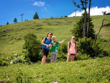 Familie beim sommerlichen Wandern, im Hintergrund Liftstützen