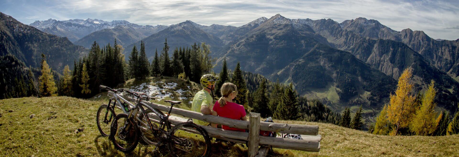 Mountainbiker machen Rast auf einer Bank mit Blick ins Tal