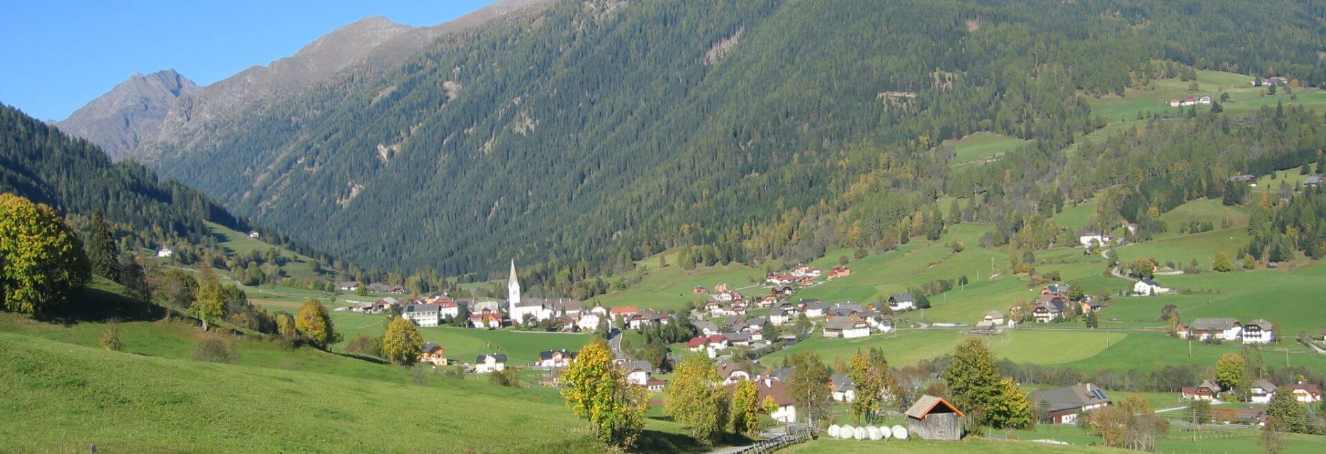 Das Dorf Lessach im Lungau bei Sonnenschein, Häuser, eine Kirche, ein Weg, ein Zaun
