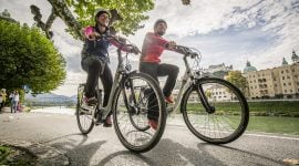 Zwei Radfahrer fahren am Ufer der Salzach auf dem Tauernradweg durch die Stadt Salzburg.