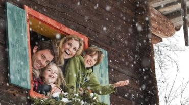 Familie beugt sich aus dem geöffneten Bauernhoffenster und freut sich über die Schneeflocken