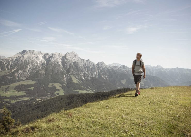 Mann beim Wandern über eine Almwiese, im Hintergrund schroffe Berge