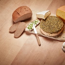 Verschiedene Käsesorten und Bauernbrot liegen neben einem Schnittlauchbrot mit Butter