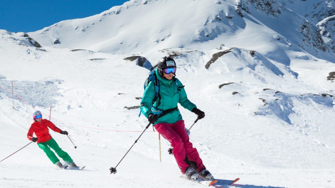 Skifahrer in türkiser Jacke und roter Hose beider Abfahrt