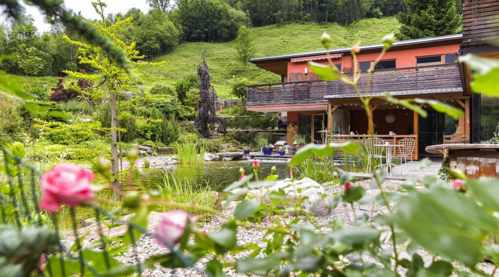 Haus mit Schwimmteich umgeben von einem blühenden Rosengarten, Wiese und Wald