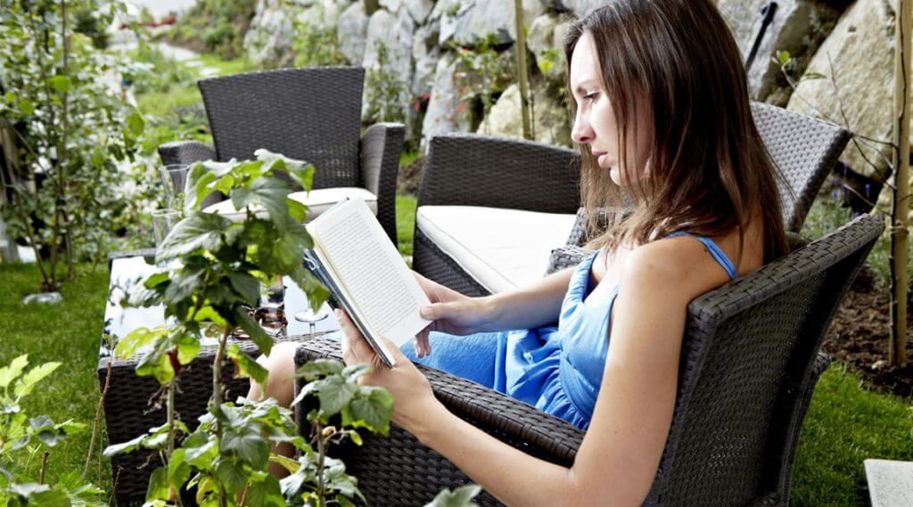 Frau in blauem Sommerkleid beim Lesen in einem Rattansessel im Garten