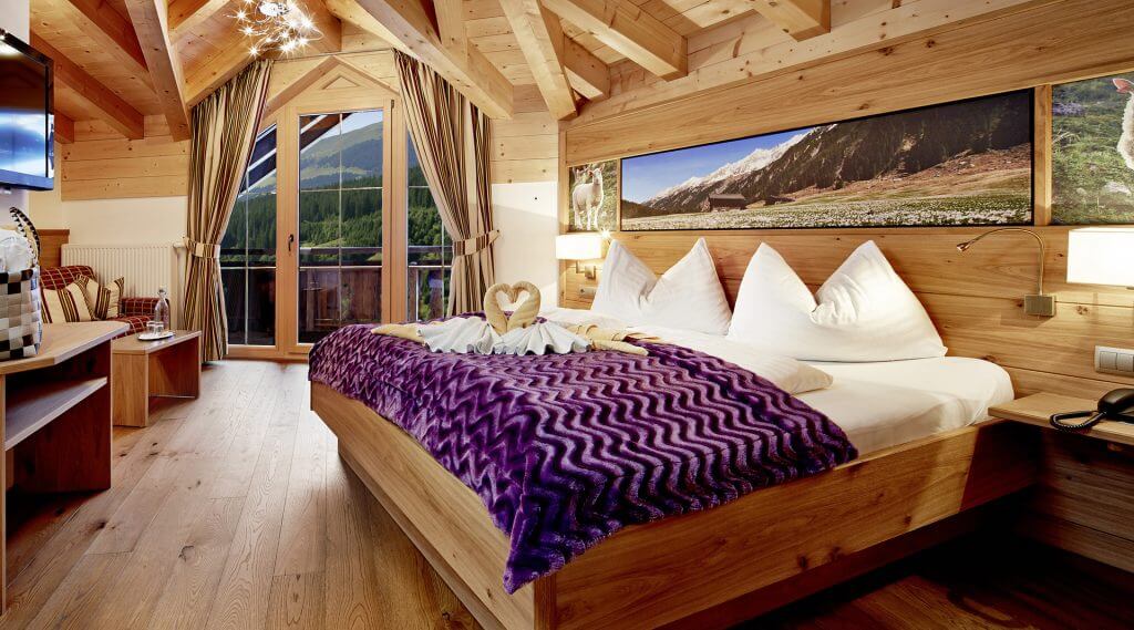 Hotelzimmer mit Einrichtung aus Naturholz, lila Bettüberwurf