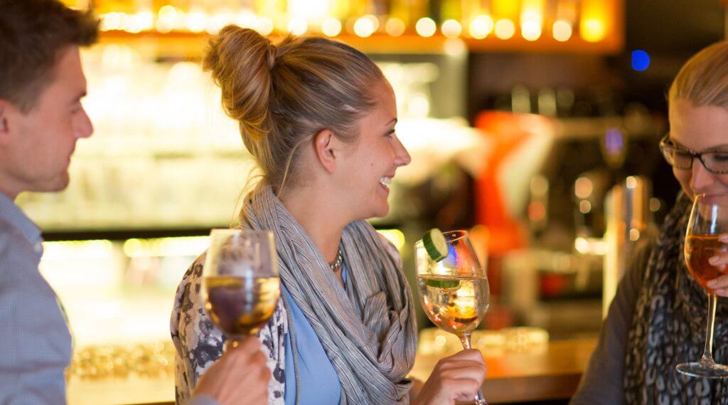 Drei junge Leute stehen mit einem Glas Wein in der Hand an der Bar