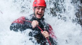Mann mit rotem Helm und Neoprenanzug unterm Wasserfall