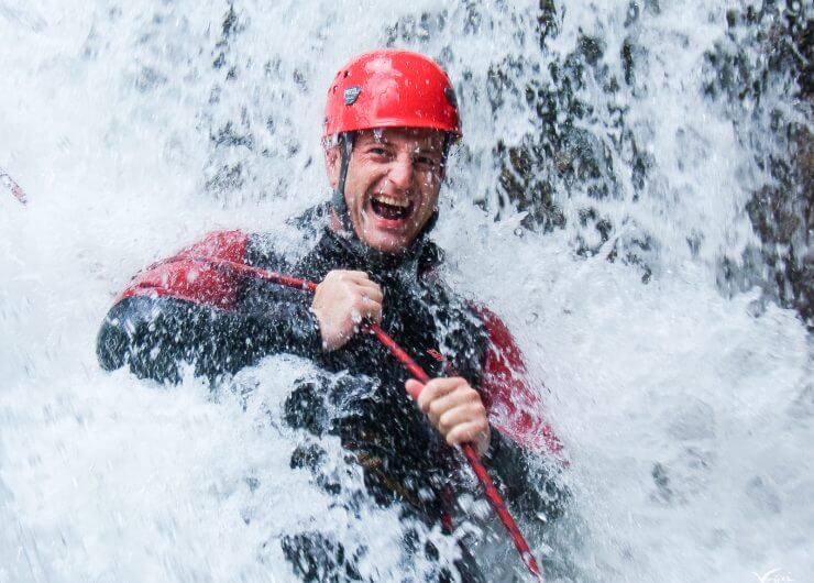 Mann mit rotem Helm und Neoprenanzug unterm Wasserfall